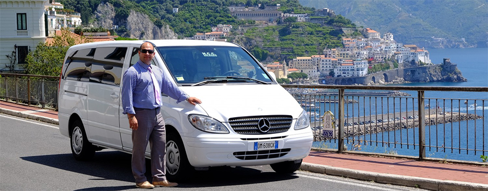 Giosy accanto al minivan NCC con vista su Amalfi